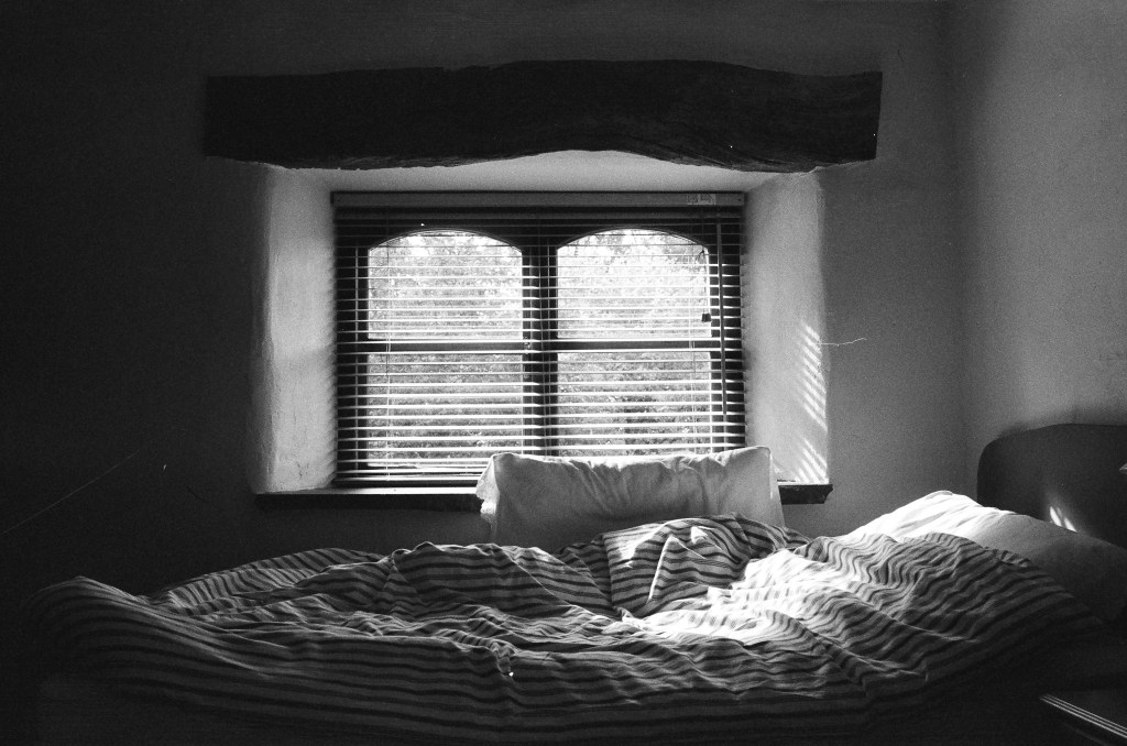 side view of a bed with stripped duvet benath a window with blinds and the light filtering through